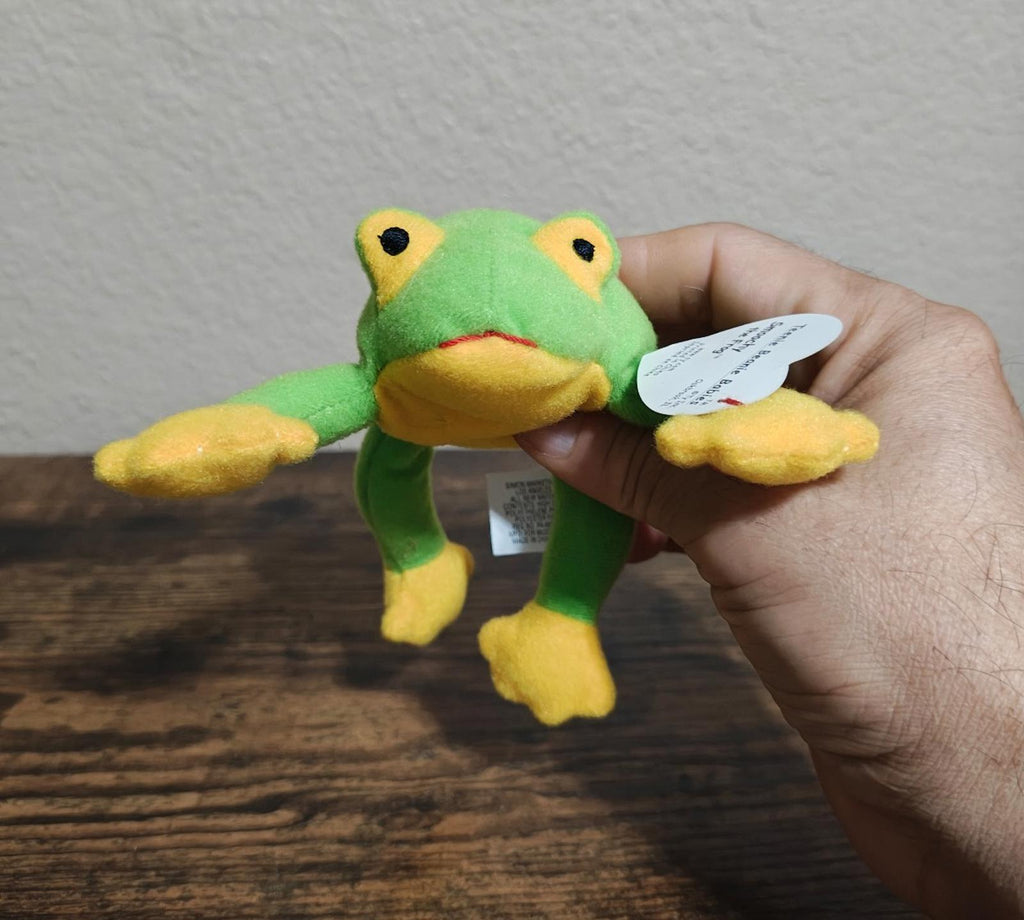 Green frog beanbag plush with yellow belly, arms, and feet, held by hand