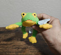 Green frog beanbag plush with yellow belly, arms, and feet, held by hand