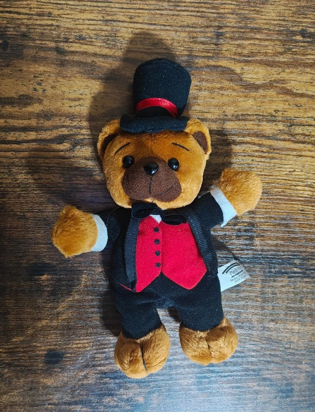Standing plush bear facing up with black top hat, red vest, and white shirt cuffs.