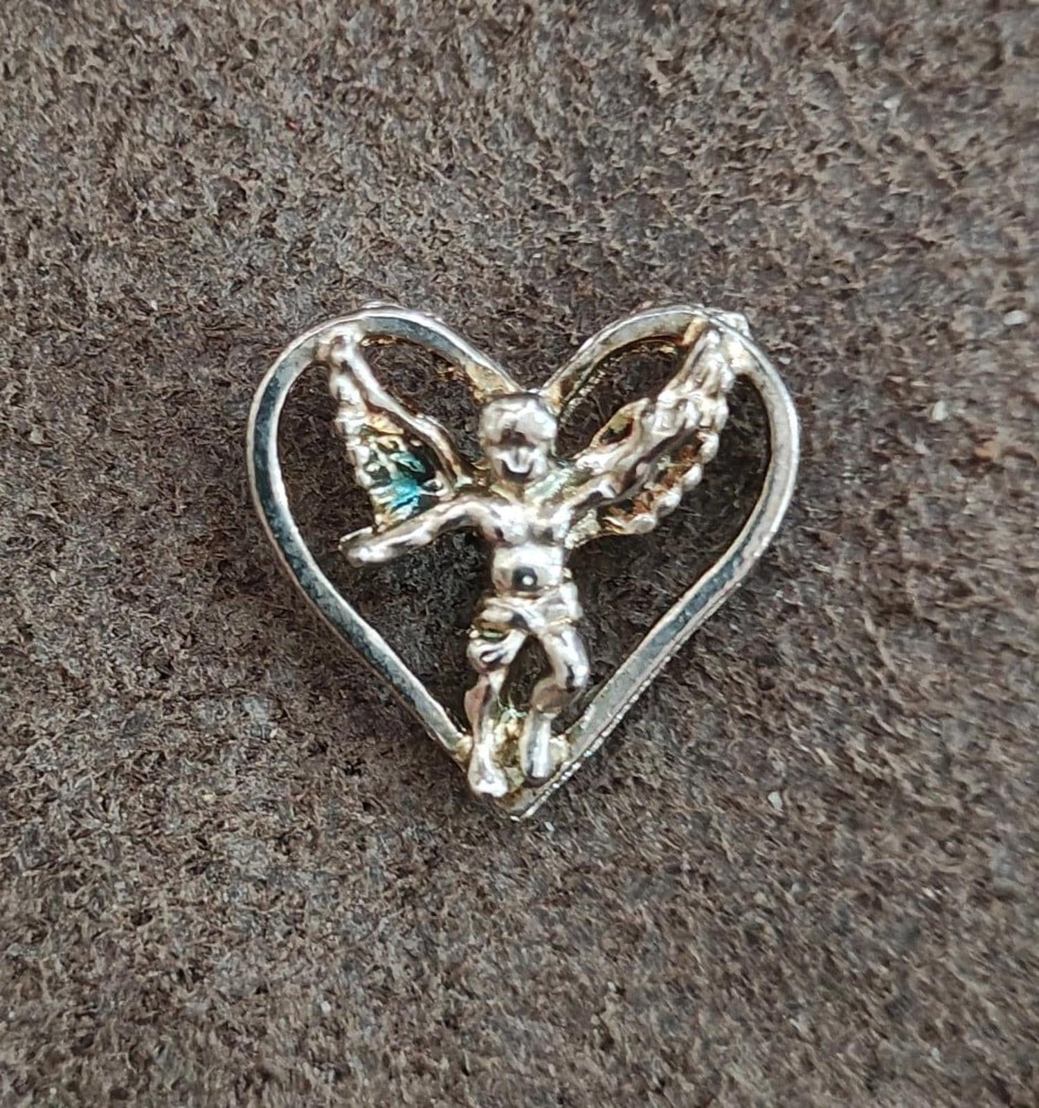 Silver-tone winged angel heart pin on dark textured background, full front view