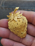 Gold tone strawberry brooch pin with raised seed texture and leaf top.