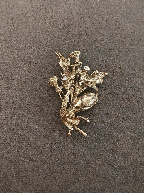 Gold-tone bagpipe player brooch with rhinestone accents, scattered thistle motifs