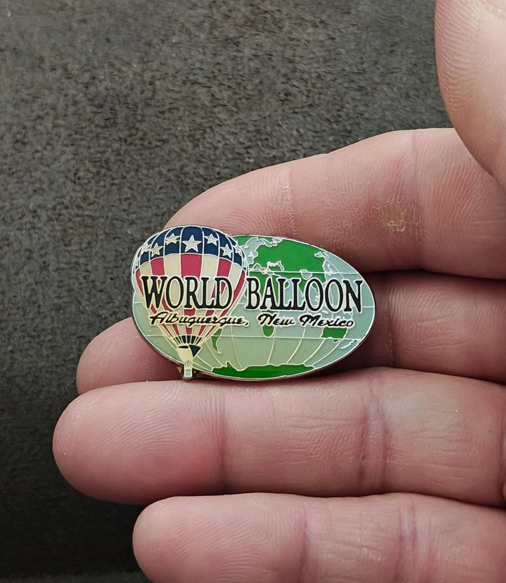 Silver-tone oval enamel lapel pin with green balloon artwork and blue stars over red stripe