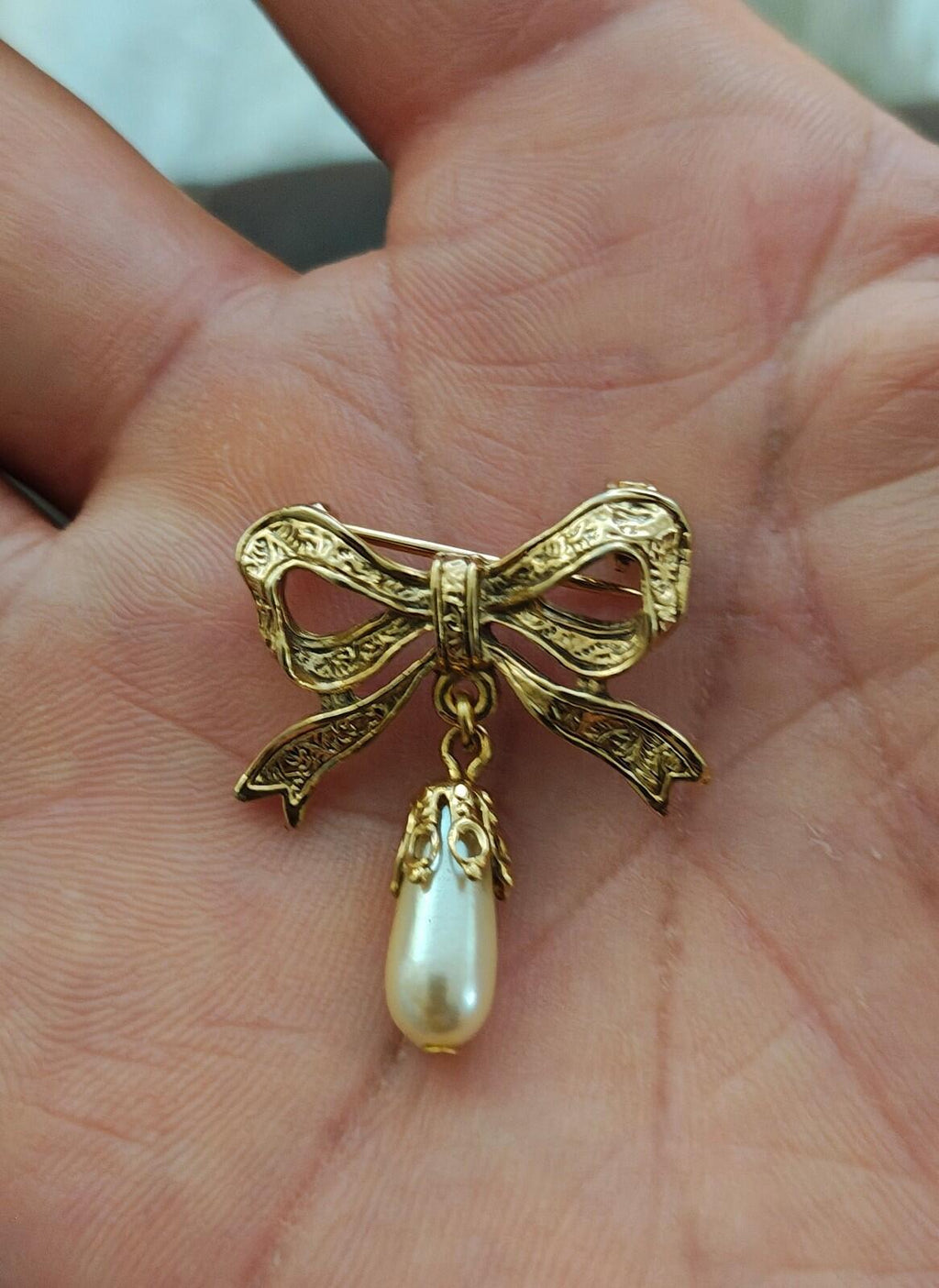 Gold bow brooch with dangling pearl drop and ornate embossed ribbon ends