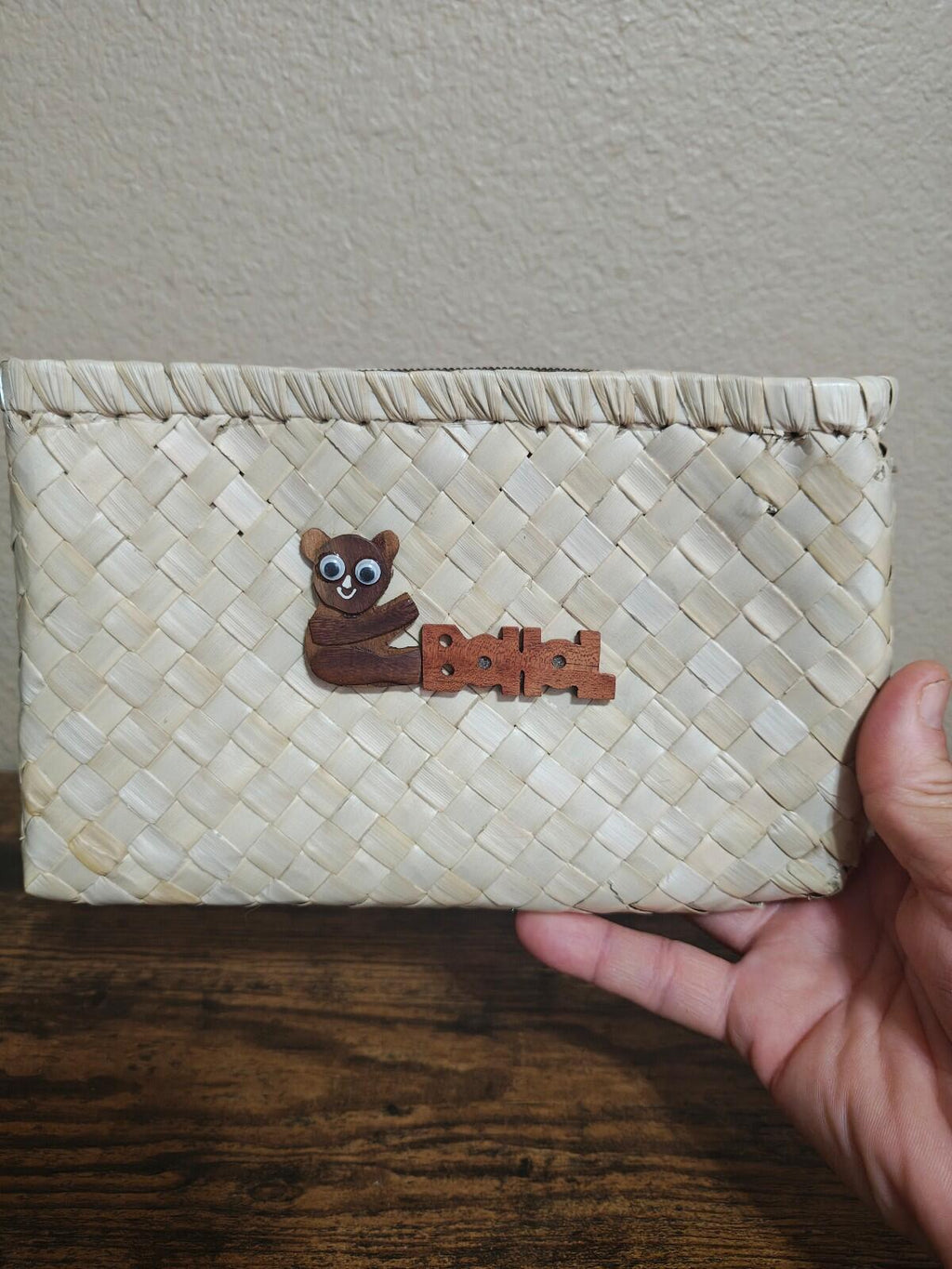 White handwoven pouch with wooden tarsier emblem, held in hand