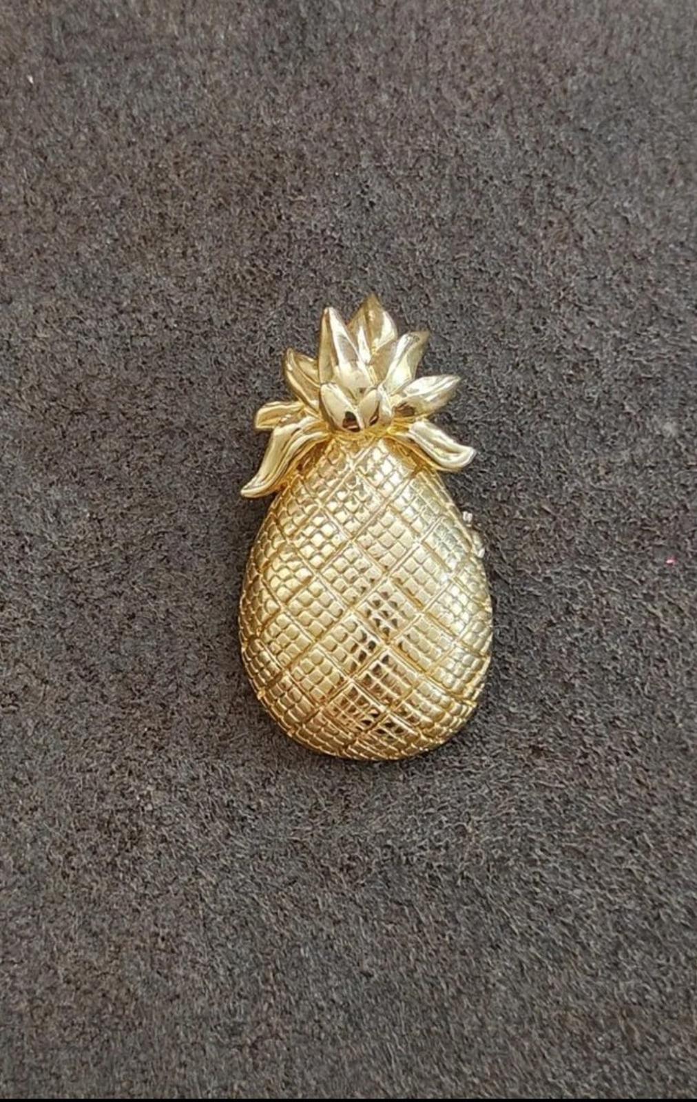 Gold tone pineapple brooch with leaf cluster and textured pineapple surface on fabric
