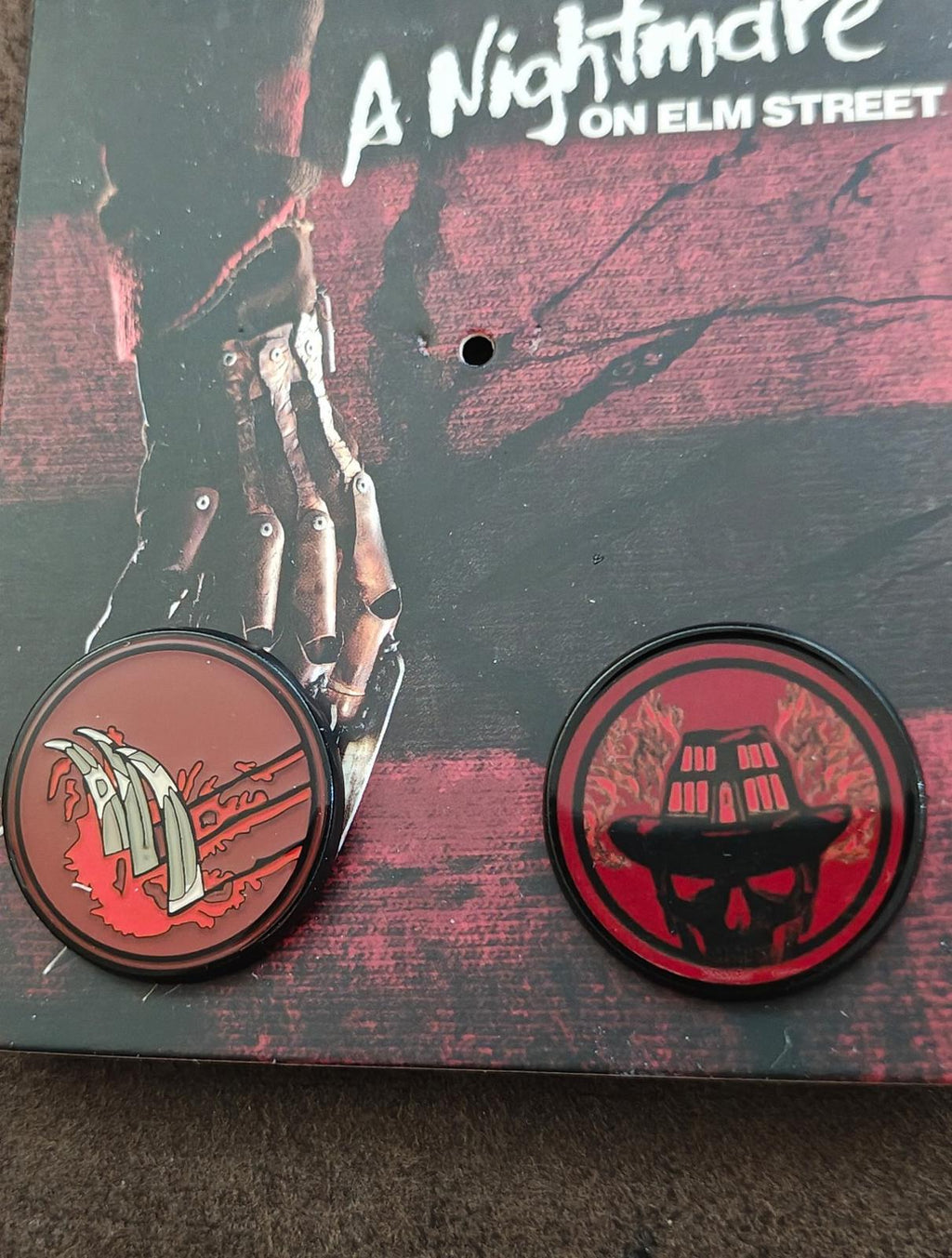 Two round enamel pins on card: left glove icon and right skull icon in red and black
