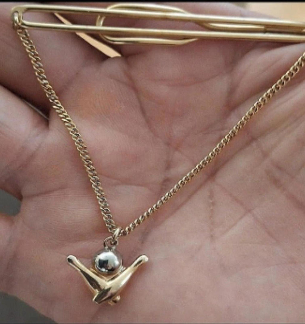 Gold-tone bowling tie bar with chain and pin charm resting across an open hand.