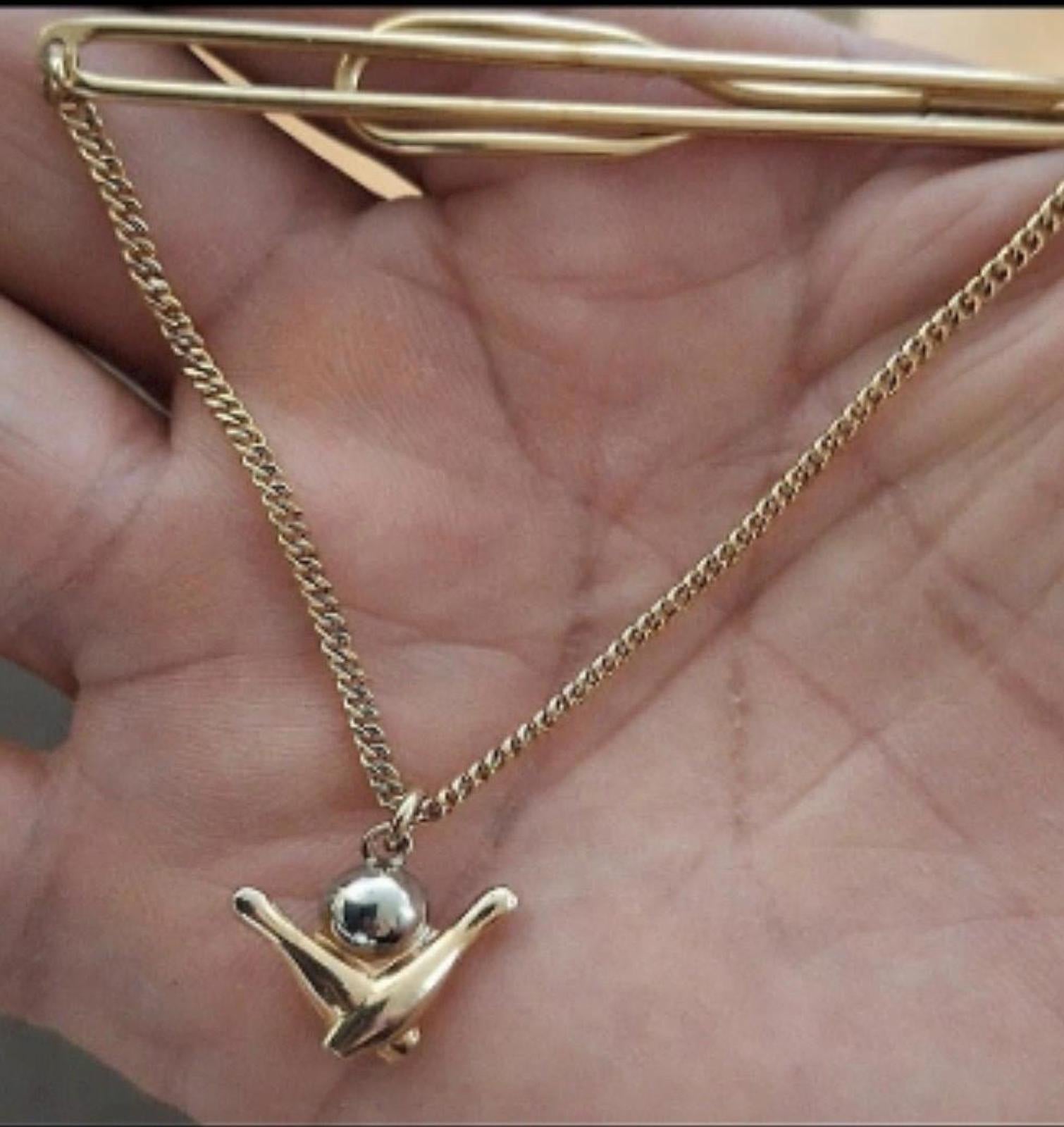 Gold-tone bowling tie bar with chain and pin charm resting across an open hand.
