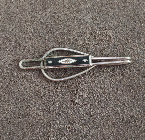Silver tone tie clip featuring black enamel shield with white starburst and loop frame