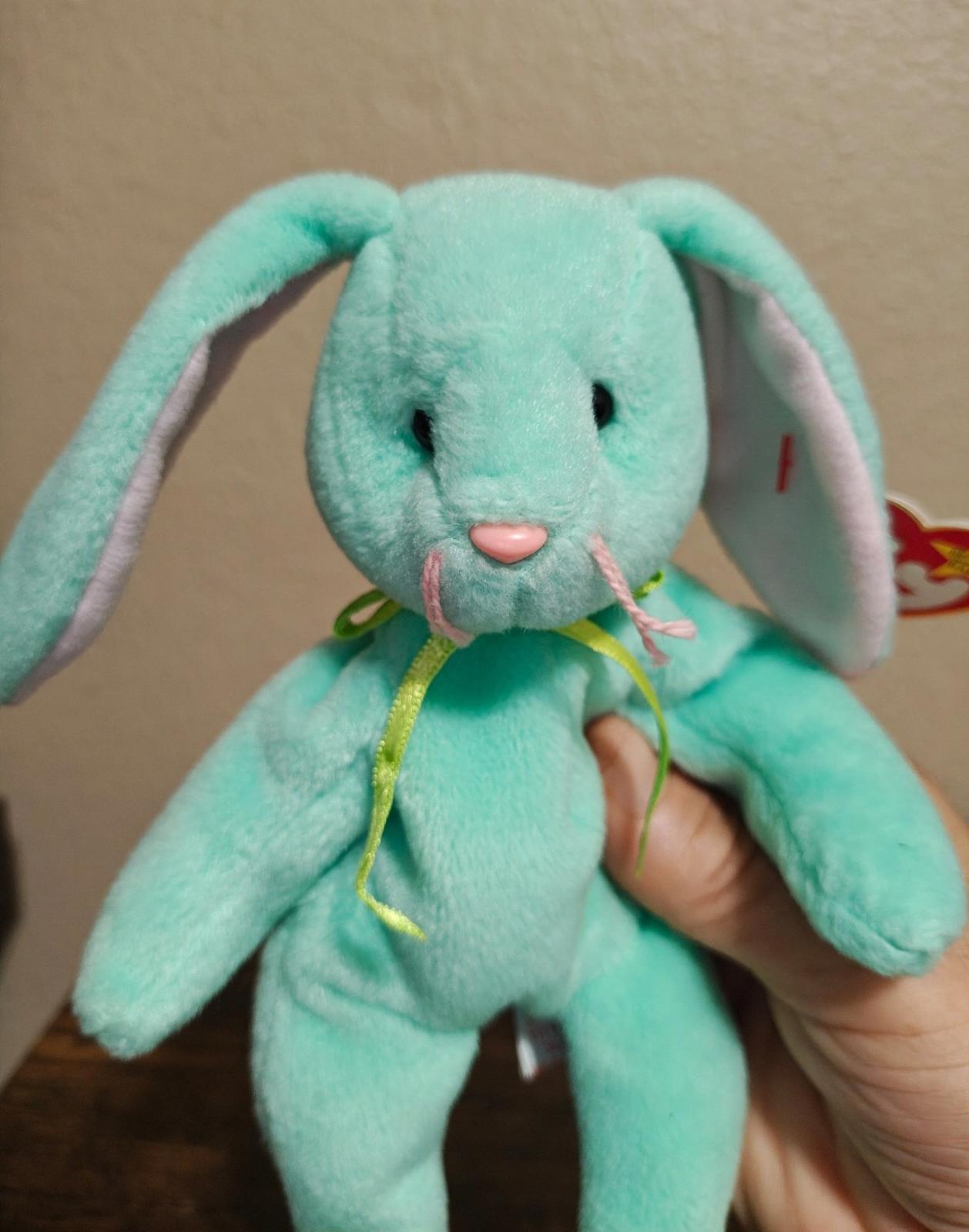 Teal plush bunny beanbag with embroidered eyes and pink nose, held up close