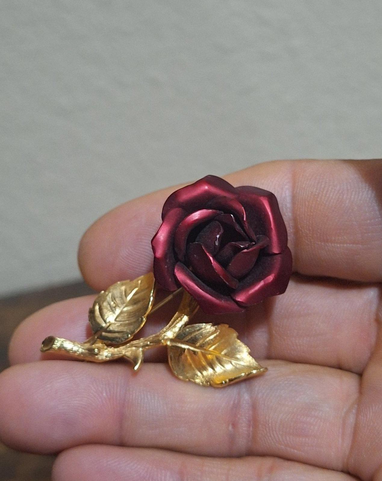 Gold-tone red rose enamel pin brooch, close-up on hand with leaf accents.