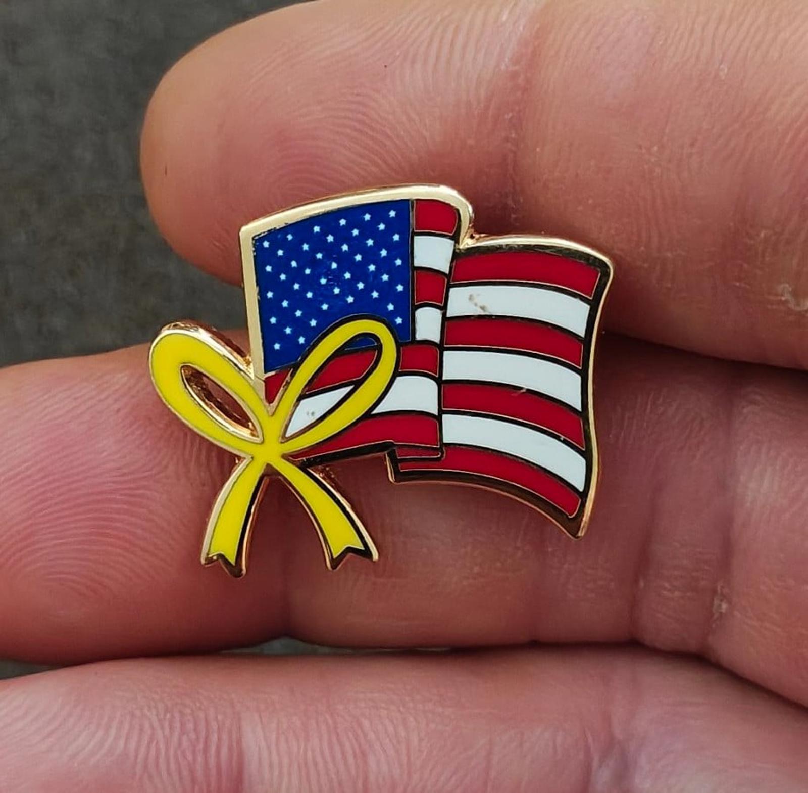 Gold-tone enamel lapel pin with wavy American flag and yellow ribbon bow