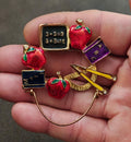 School-themed enamel brooch with red apple charms, books, pencil, and chalkboard plaque.