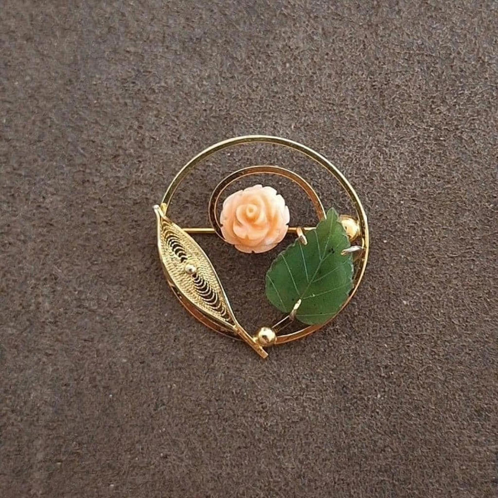 Gold-tone circular filigree brooch featuring a pale rose and two green leaves.