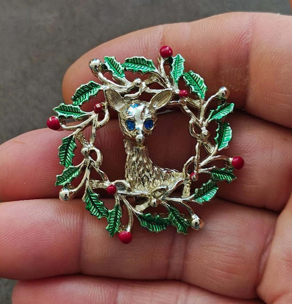 Gold tone enamel reindeer brooch in a holly wreath with green leaves and red berries