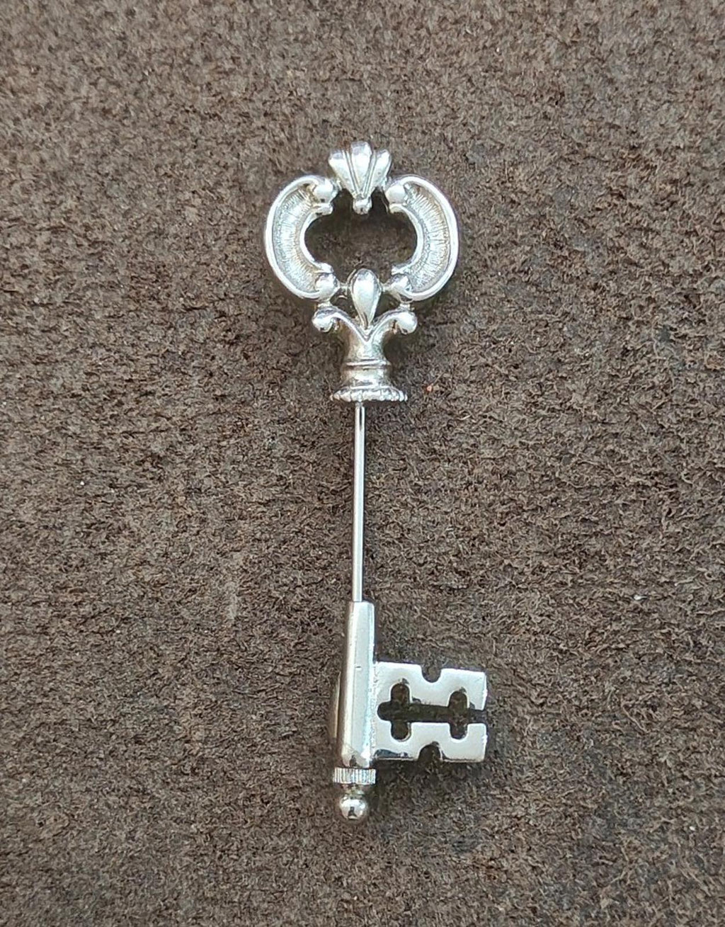 Silver stick pin with fleur-de-lis top and skeleton key charm, centered view.