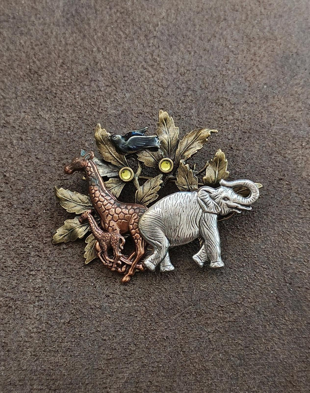 Safari animal brooch with silver-tone elephant, greenish bird, and leaf accents in mixed metals