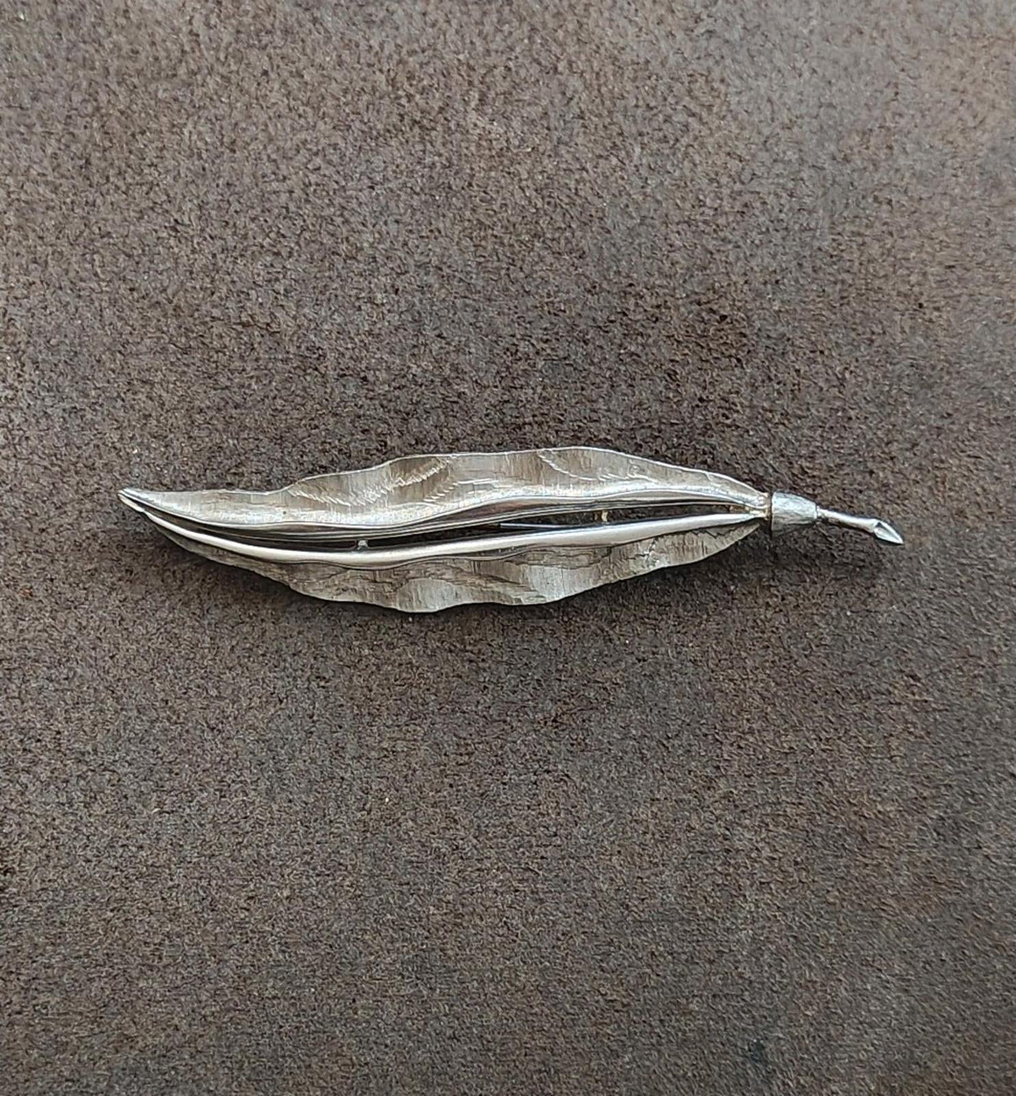 Silver tone leaf brooch lying flat, hammered surface with pointed edges and clasp