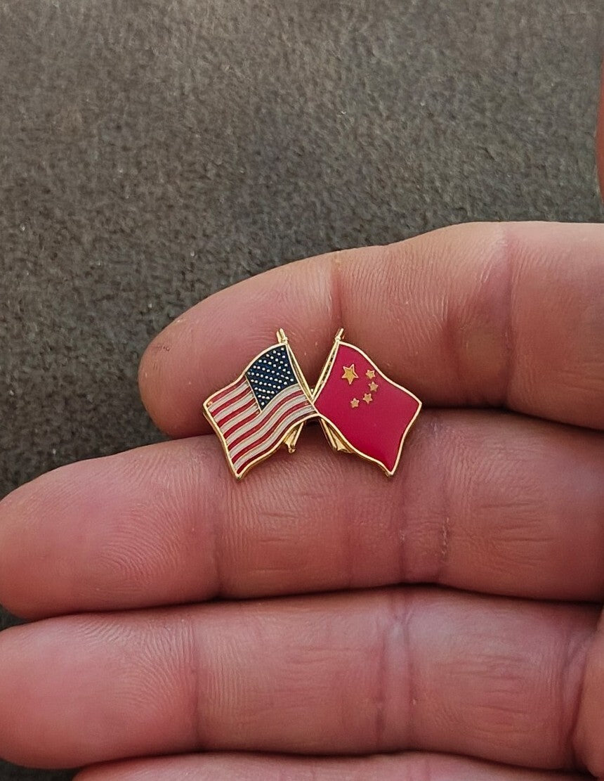 Small gold tone enamel pin of crossed US and China flags on a hand.