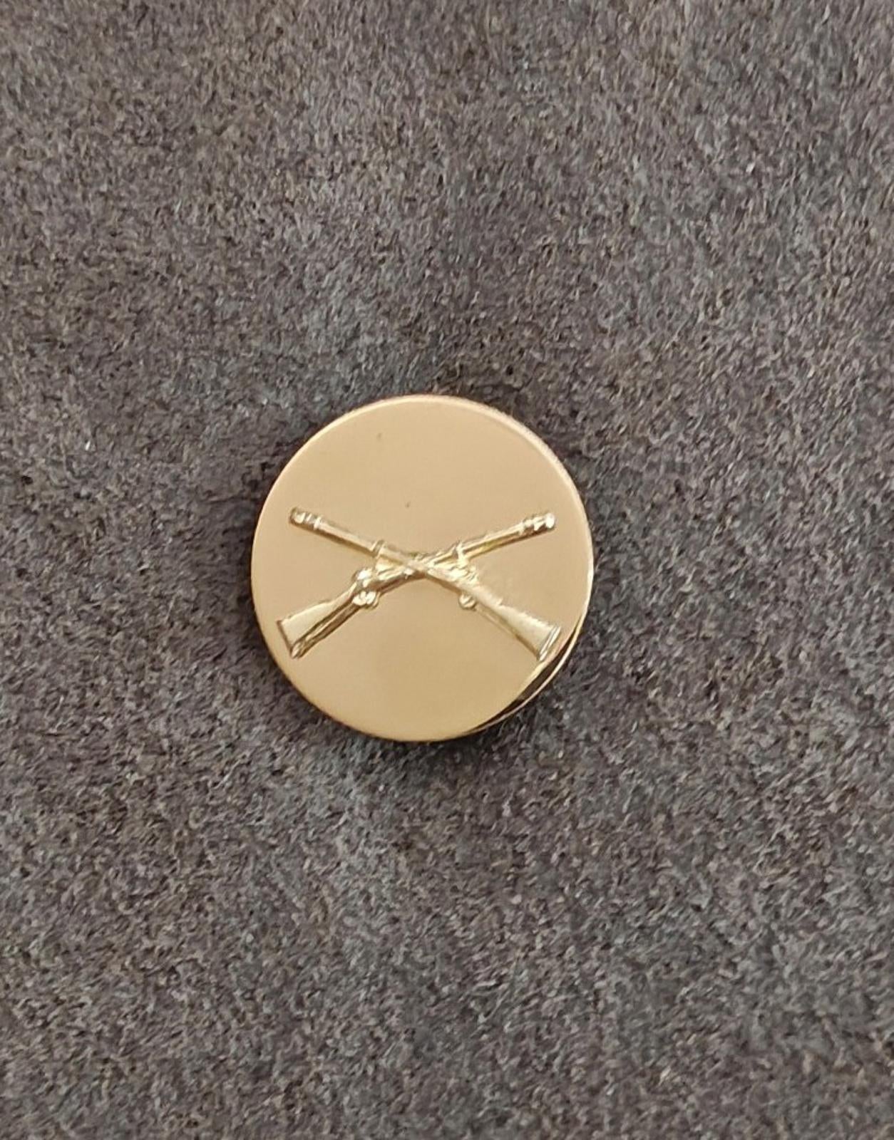 Gold circular brass pin with crossed rifles emblem, small front view