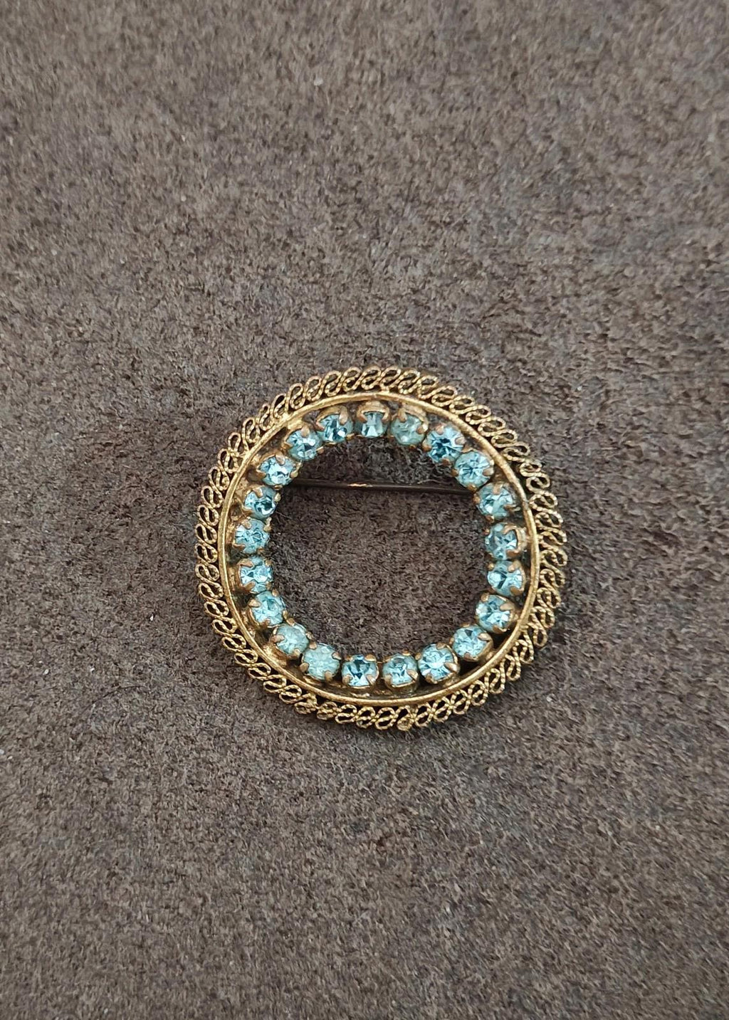 Round gold-tone brooch with blue stone circle and scalloped filigree border