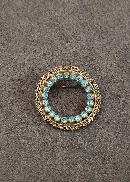Round gold-tone brooch with blue stone circle and scalloped filigree border