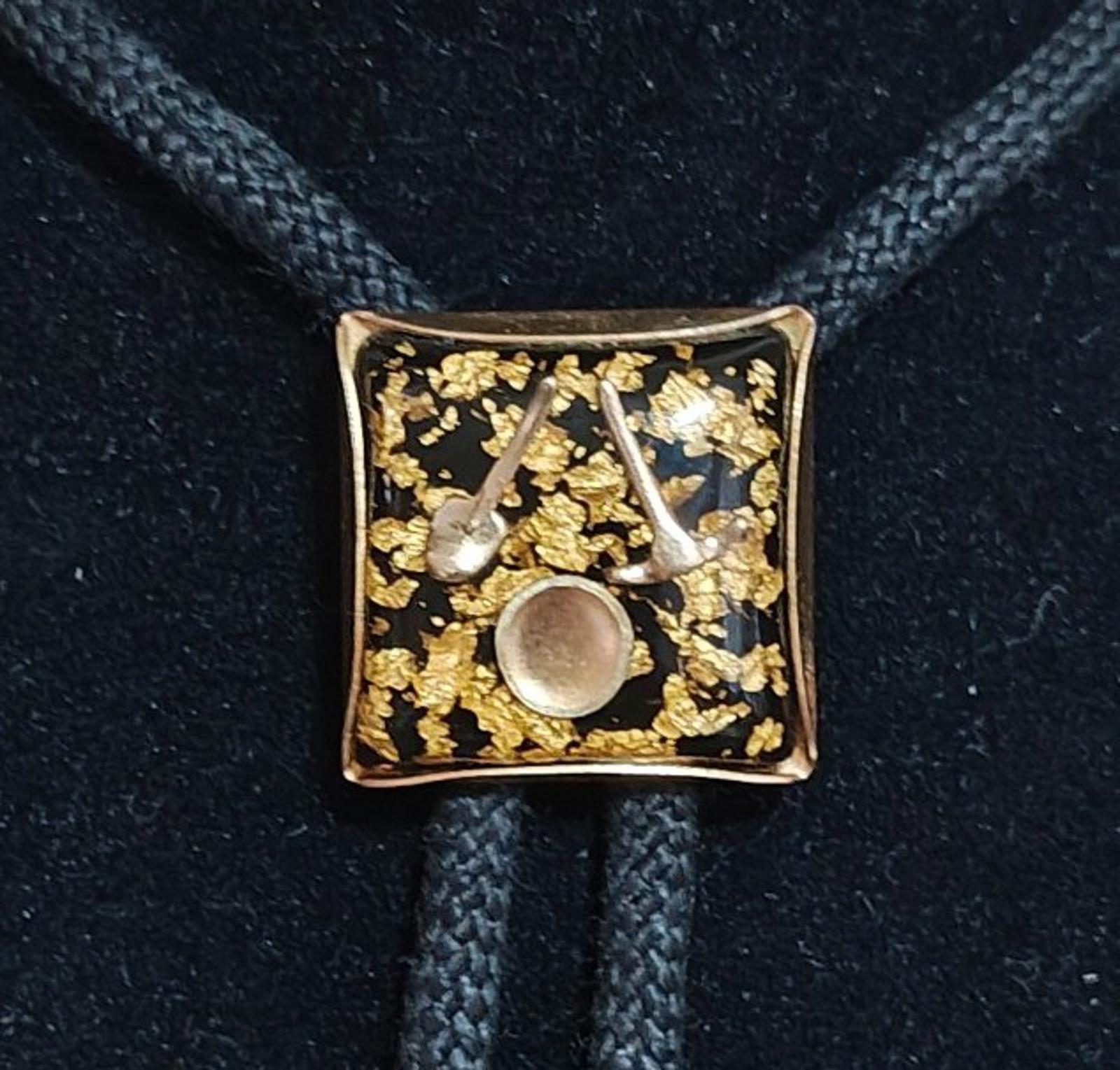 Close-up of gold square bolo pendant with circular inlay and scattered gold flecks on black