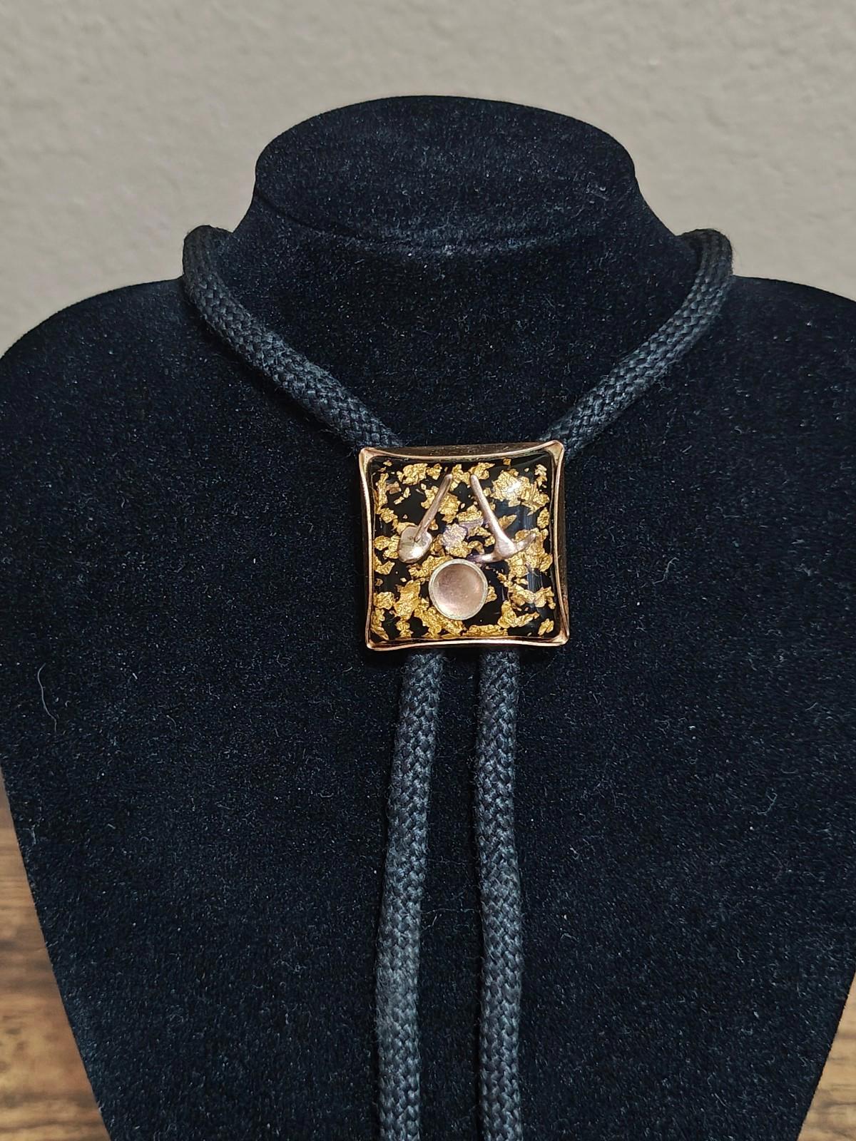 Black bolo tie with gold square lucite-style pendant filled with gold flecks and a miner motif