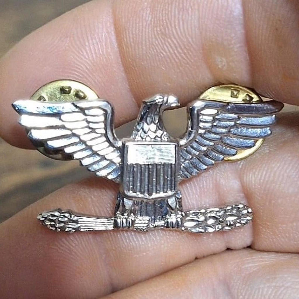 Silver-tone eagle rank pin with spread wings and central shield detail, gold accents
