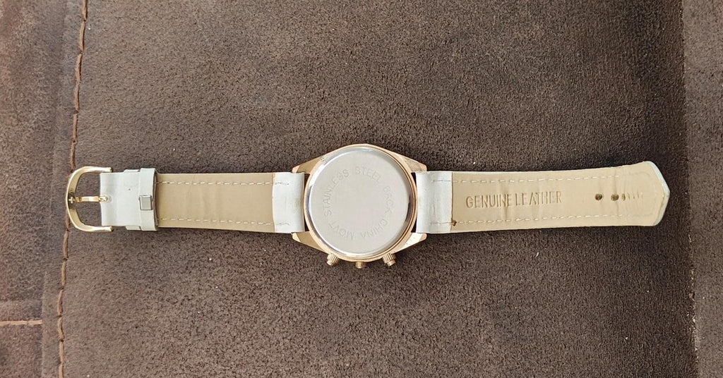 White leather watch strap with buckle and gold-tone case back, engraved text
