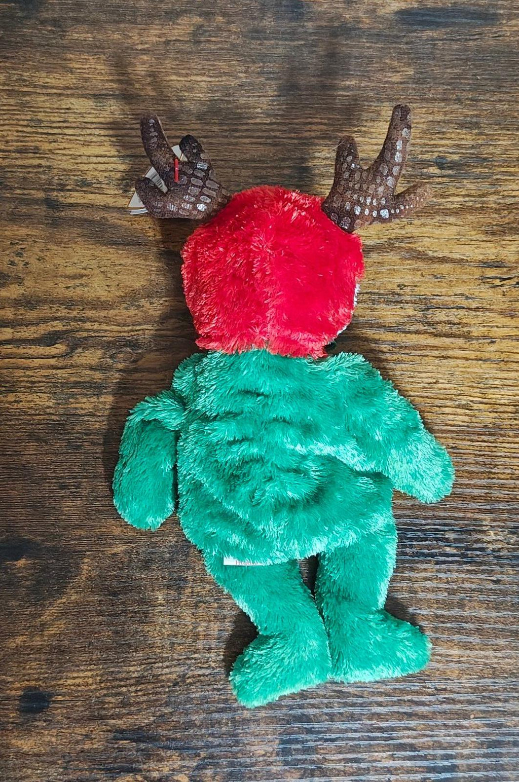 Green plush reindeer teddy bear with red head and antlers, viewed from behind
