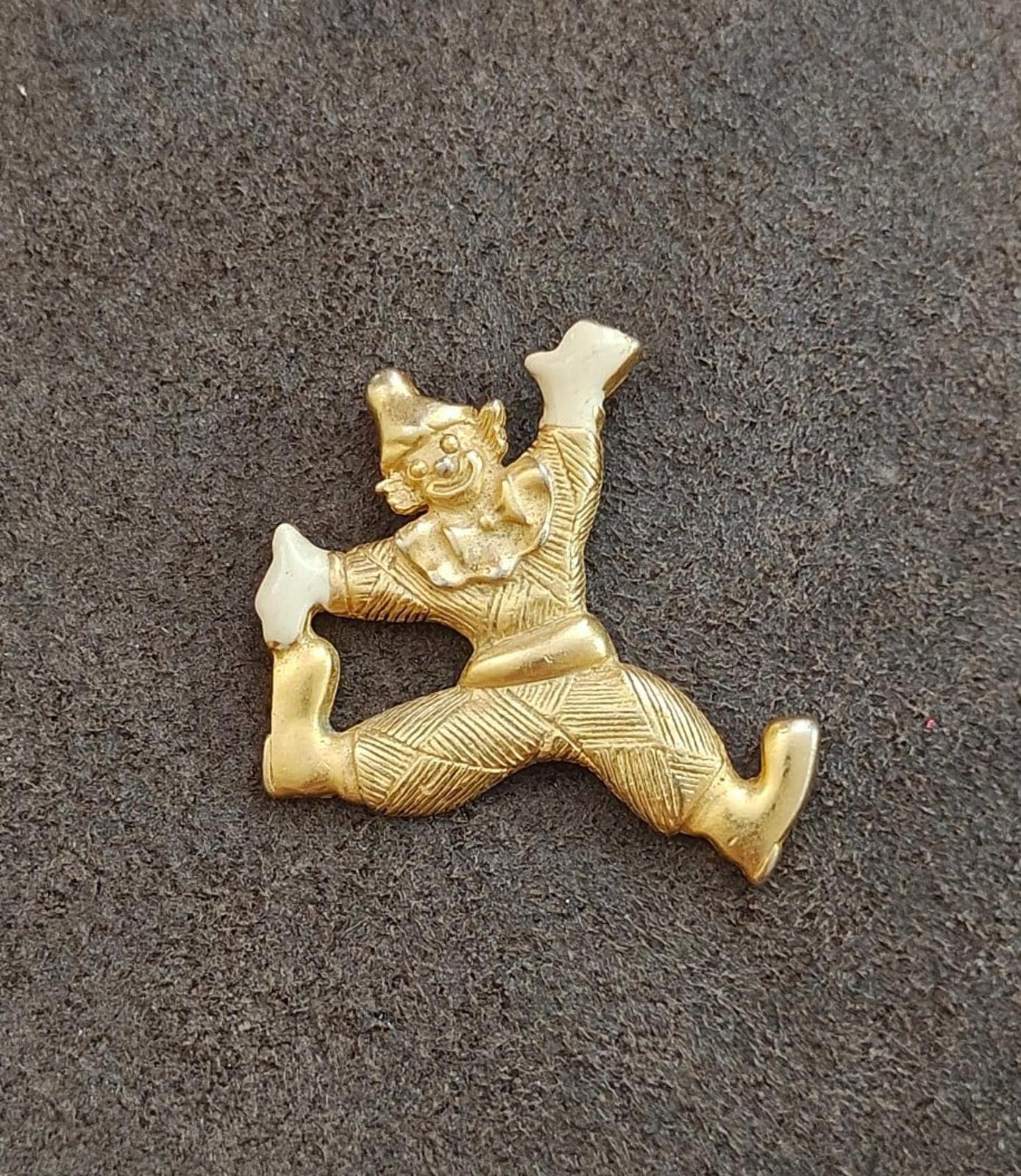 Gold tone clowning around pendant with white enamel shoes and hands, side view on gray background
