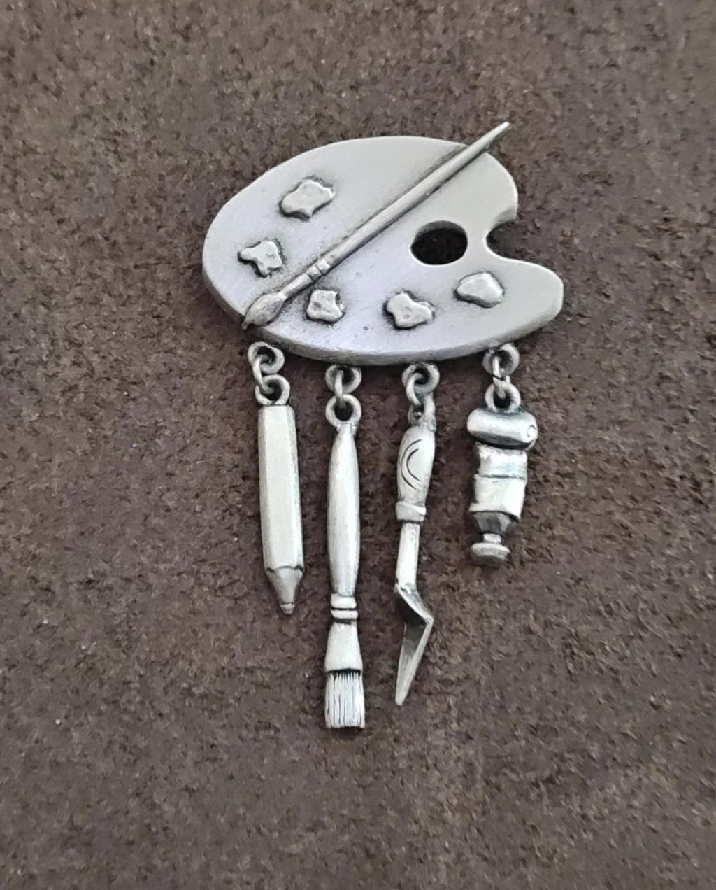 Silver-toned palette brooch with dangling paint tools and brush-shaped charms, pin