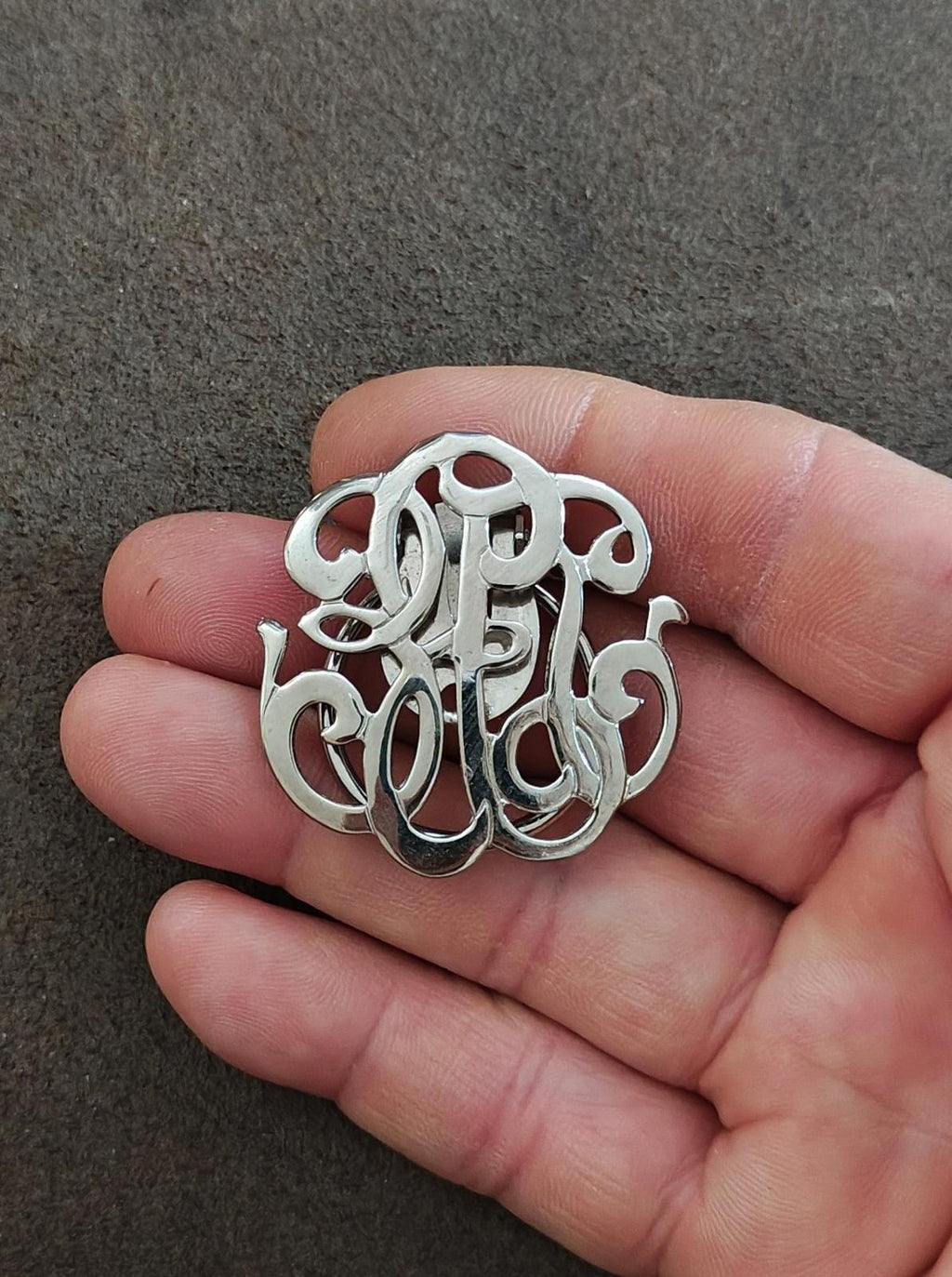 Silver-tone monogram scarf clip with decorative cutout lettering on a rounded frame