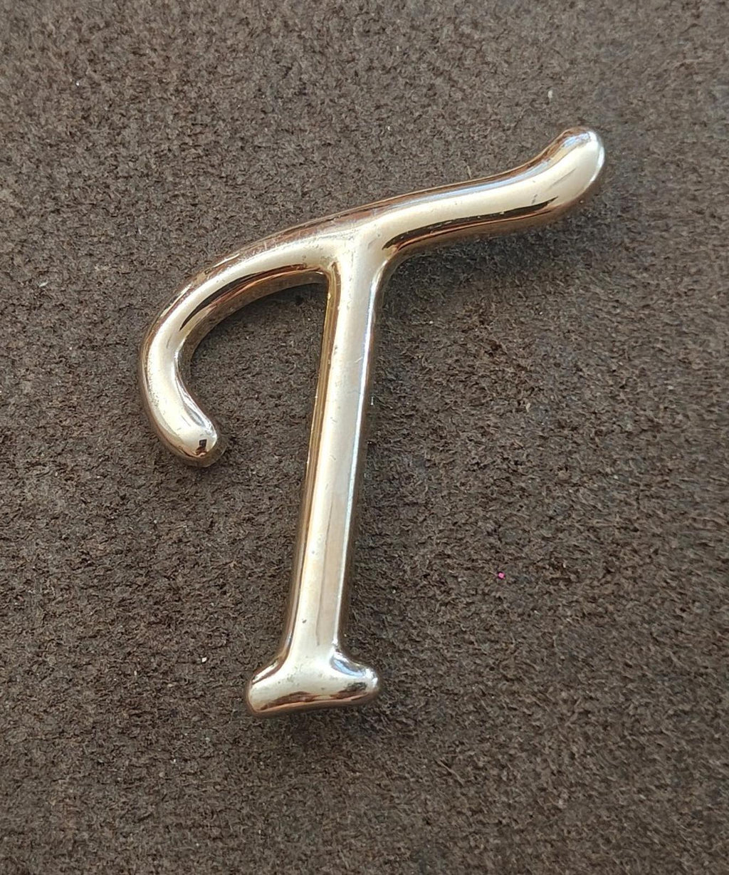 Silver-tone letter T pin/brooch on flat surface, front view