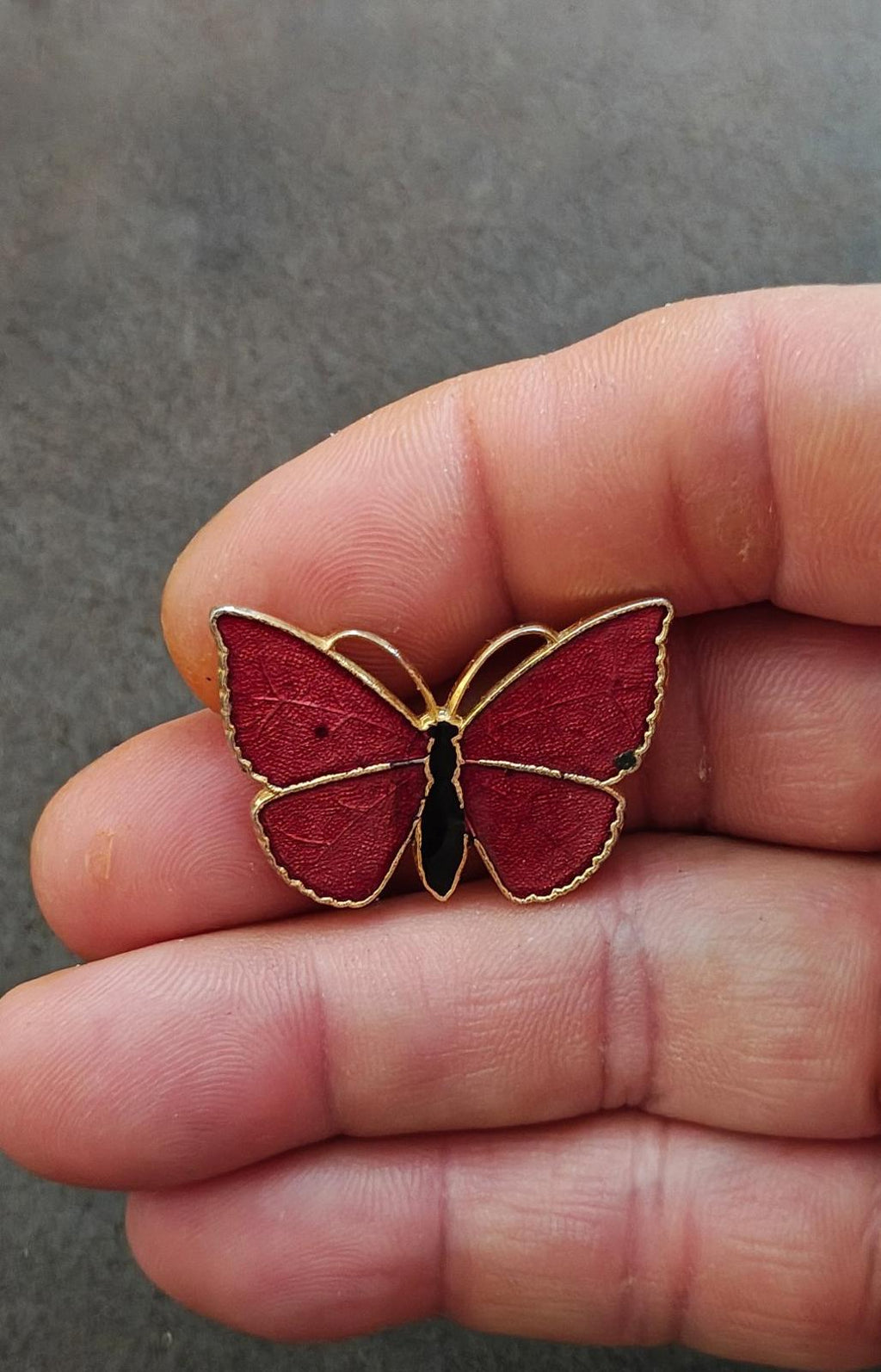 Red butterfly enamel brooch with gold-tone outline and black body, close-up in hand.