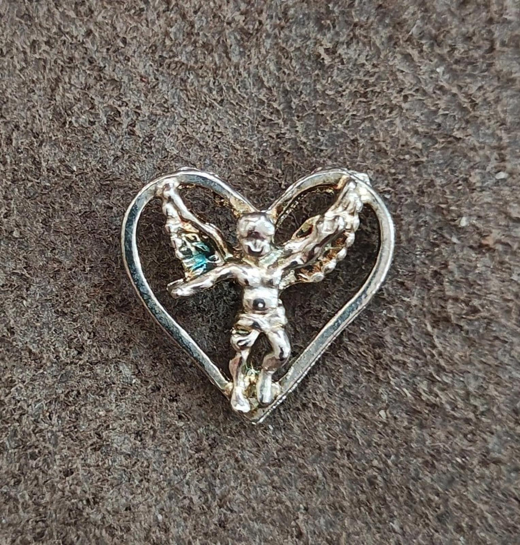 Silver-tone heart pin with winged angel figure, centered view on dark textured surface