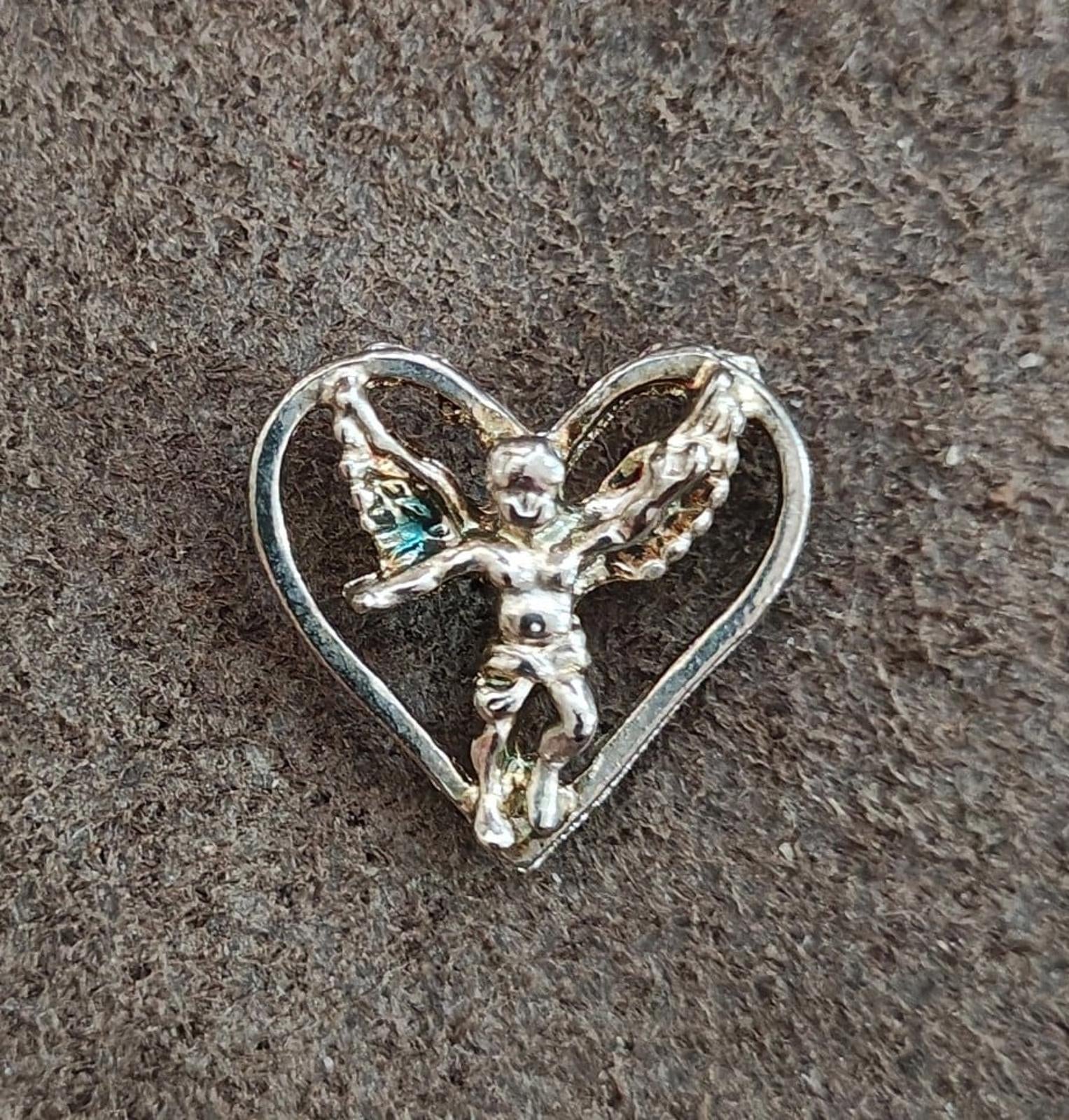 Silver-tone heart pin with winged angel figure, centered view on dark textured surface