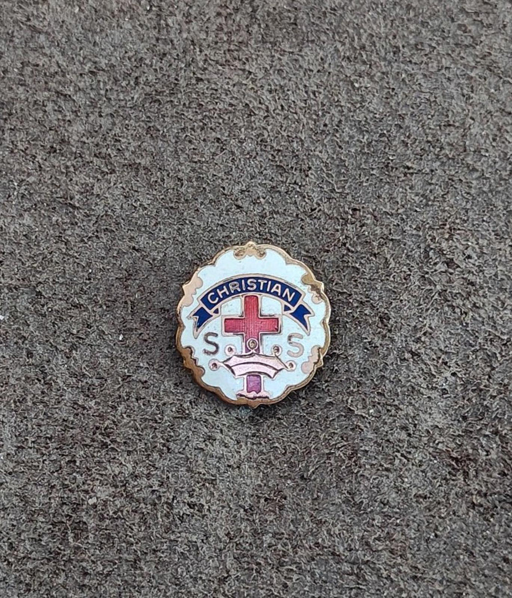 Small round Christian enamel pin with gold edge, red cross, and blue “CHRISTIAN”