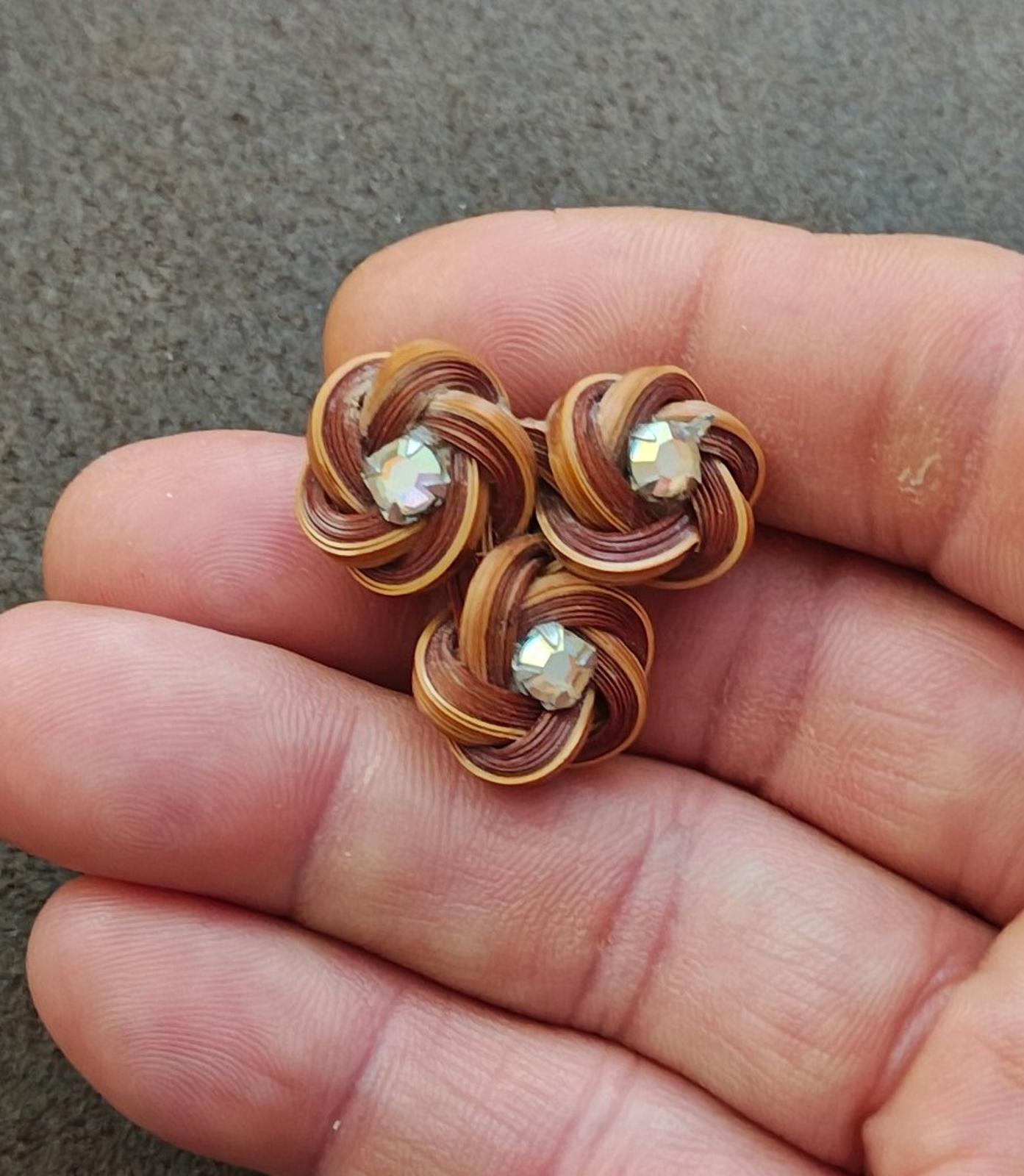 Three-flower bamboo rosette brooch with rhinestone centers, shown in hand on brown thread coils
