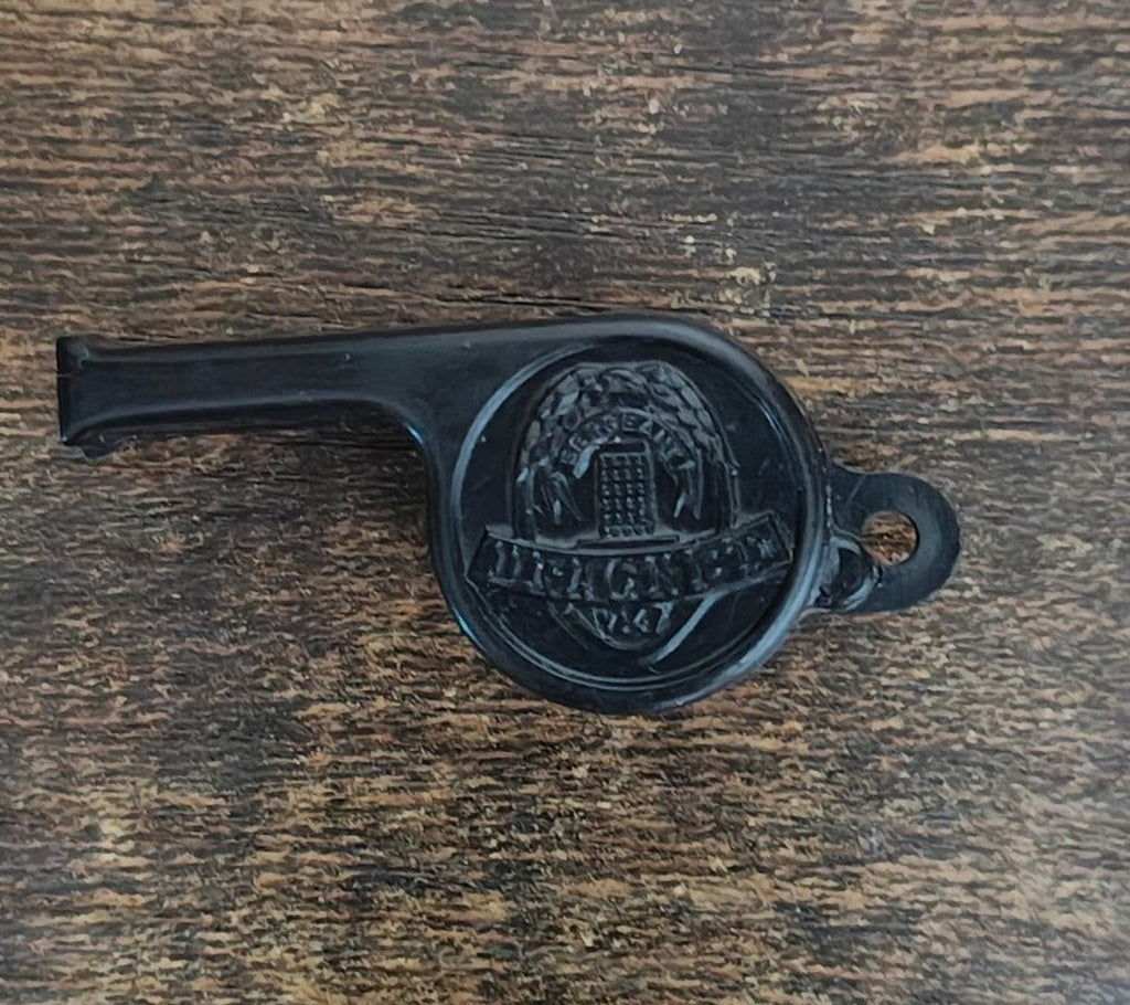 Black whistle with engraved round emblem and mouthpiece, placed on wood.