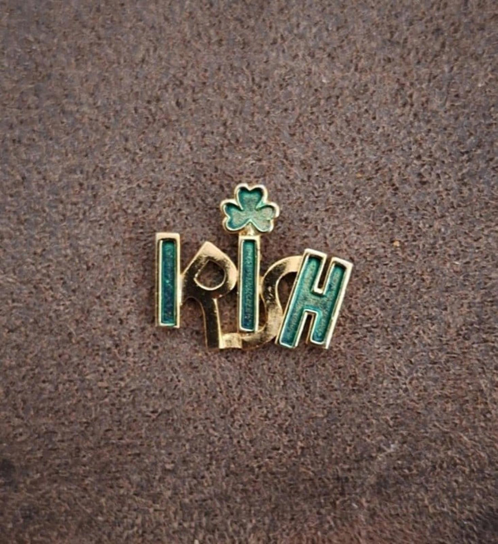 Gold-tone enamel Irish pin with green shamrock, centered on textured gray background.