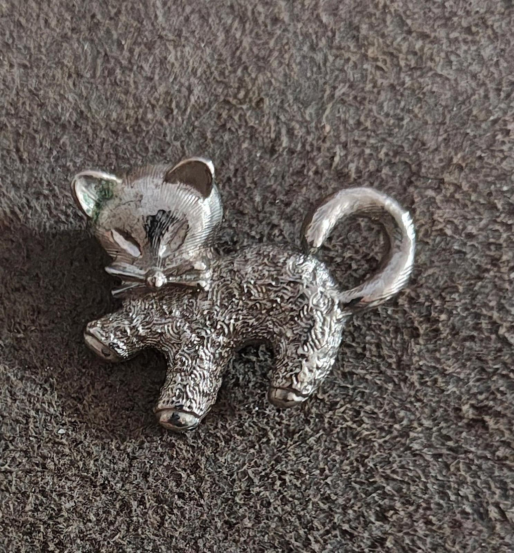 Silver-tone cat brooch pin with curled tail and bow detail, textured surface.