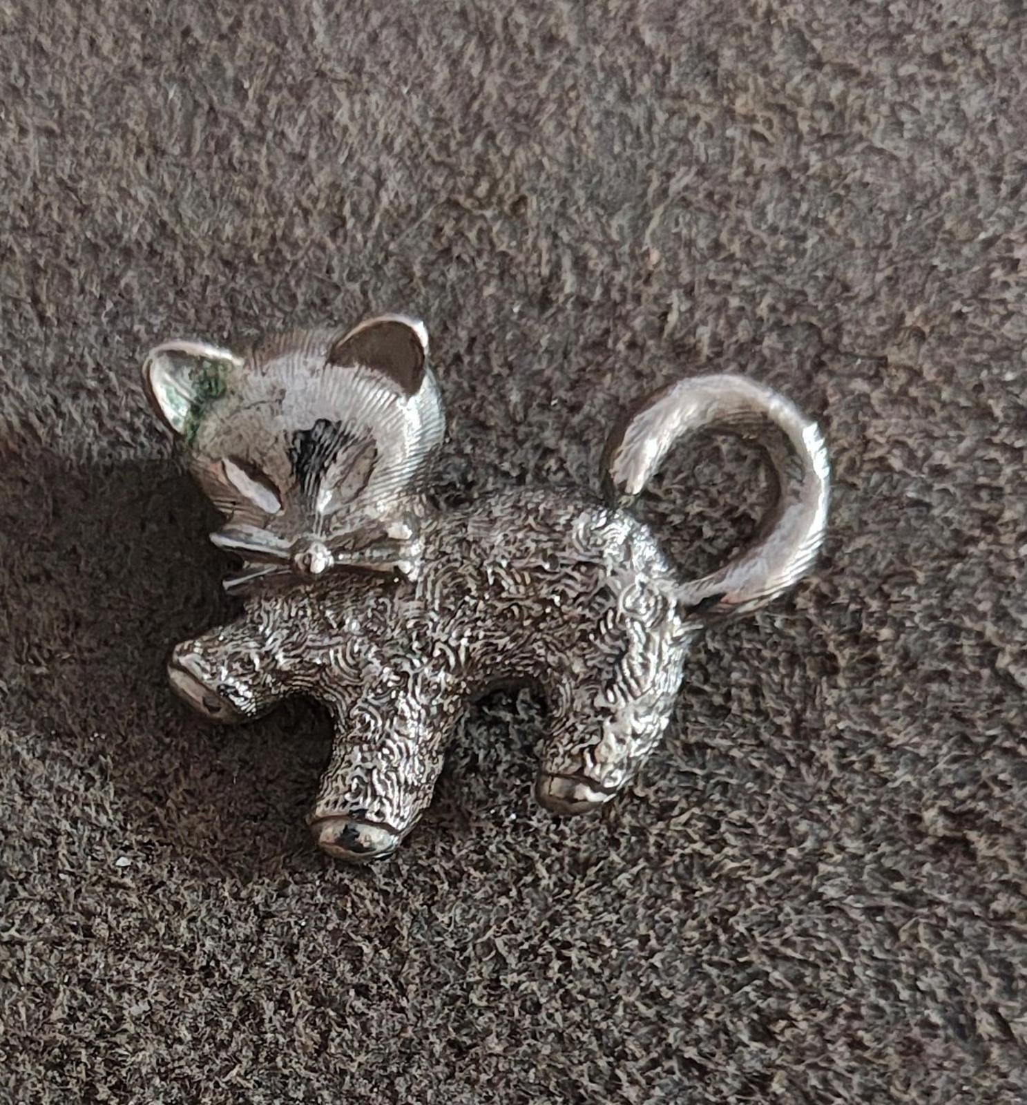 Silver-tone cat brooch pin with curled tail and bow detail, textured surface.