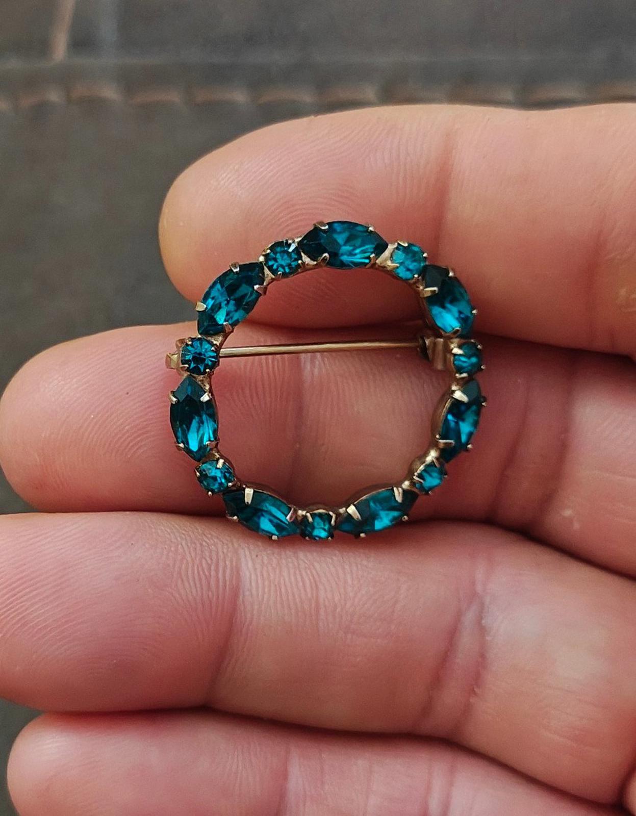 Aqua blue rhinestone circle brooch pin with gold-tone backing, close-up on fingers