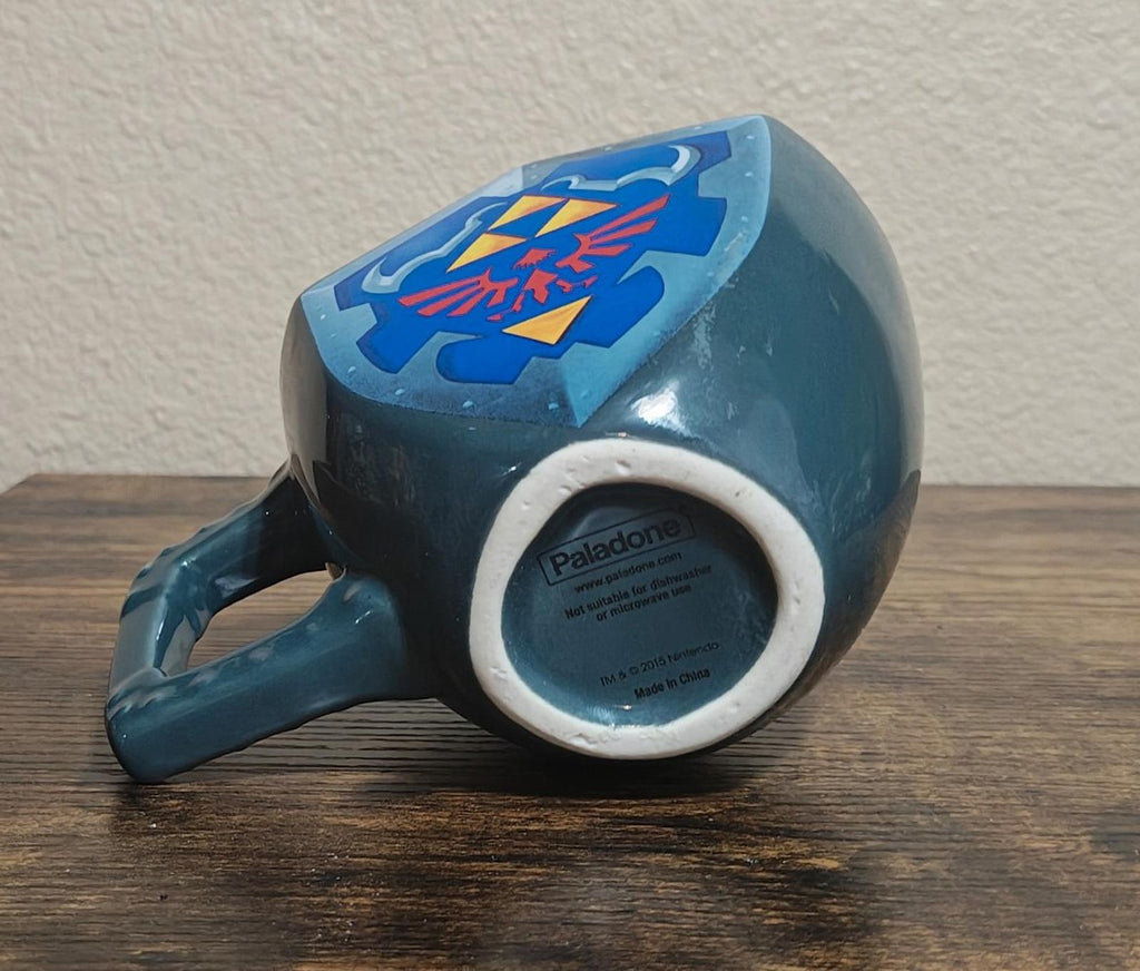 Blue mug with Hylian shield graphic and bottom stamp around the base.