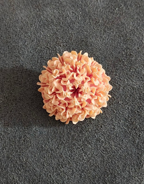Carved orange pastel flower brooch with scalloped petal edges on dark fabric