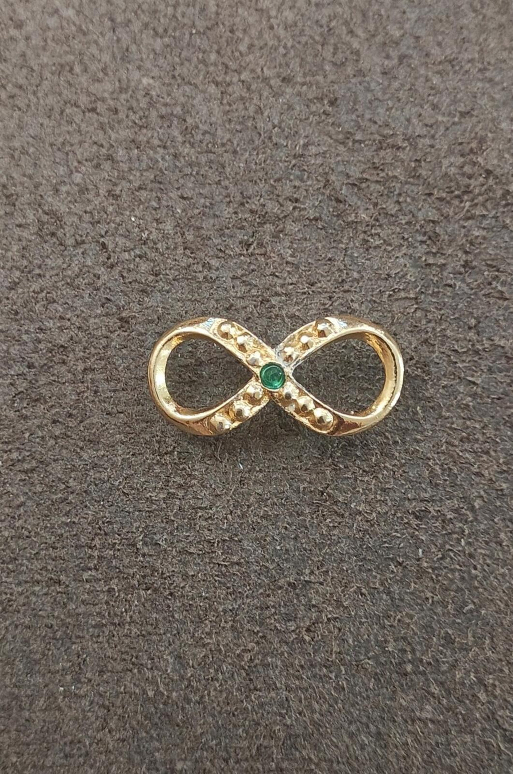 Gold infinity brooch with green emerald center and clear stone detailing