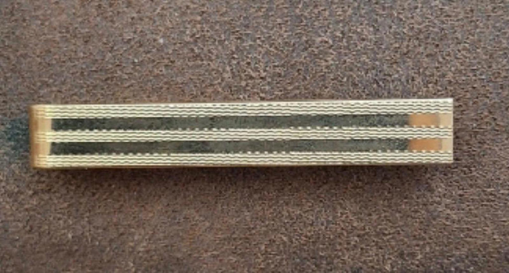 Gold tone striped tie bar clip lying flat on dark fabric